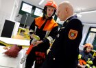 Schüler in Feuerwehrkleidung mit Feuerwehrteil bespricht etwas mit Lehrer in Feuerwehruniform
