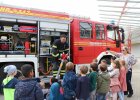 Feuerwehrmann mit Schlauch am Feuerwehrauto, zuschauende Kinder von hinten