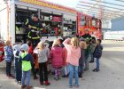 Feuerwehrmann mit Schlauch am Feuerwehrauto, zuschauende Kinder von hinten