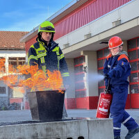 Mit dem Feuerlöscher ein echtes Feuer bezwingen, mit der Rettungsschere Fahrzeuge aufschneiden oder den Atemschutz-Parcours meistern und das in echter Ausrüstung – schnell sind die Schülerinnen und Schüler mit Begeisterung dabei. Feuerwehrmann und Kind bei Feuerlöschübung