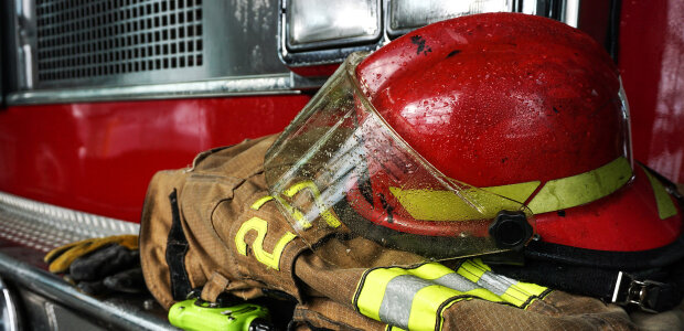 - © iStock/Matt277 Nahaufnahme: Helm auf Feuerwehrkleidung vor Feuerwehrauto